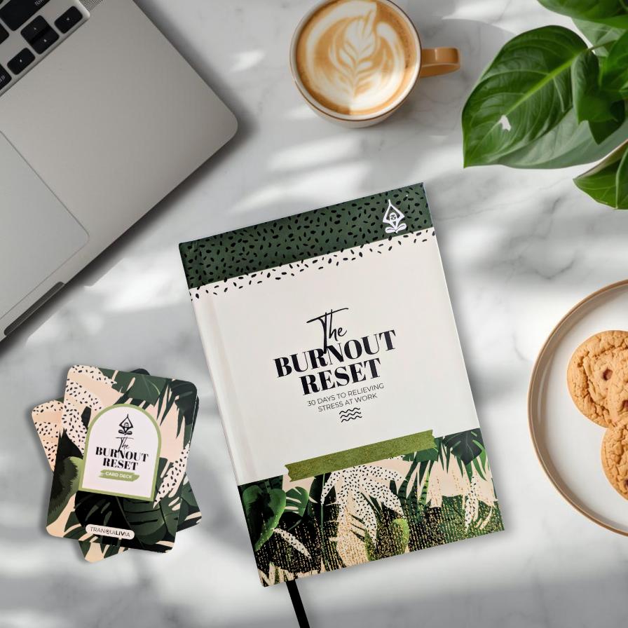 Book titled 'The Burnout Reset' and mindful card deck called 'The Burnout Reset' on a table with a laptop, coffee, cookies, and a plant.