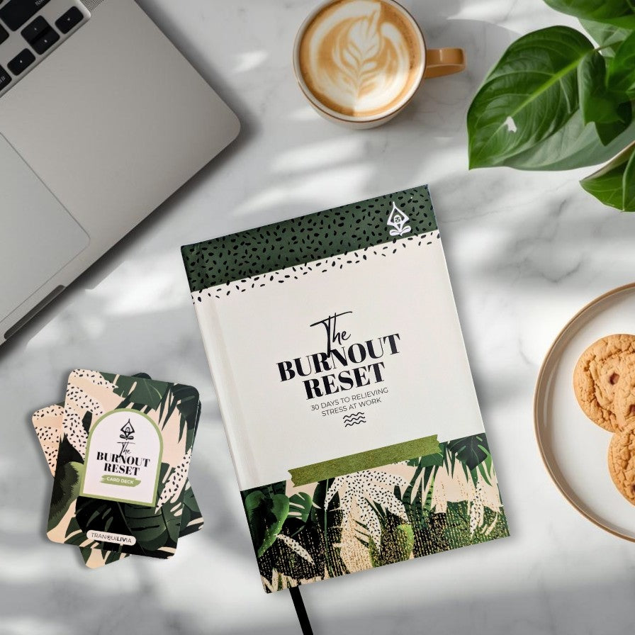 Book titled 'The Burnout Reset' and mindful card deck called 'The Burnout Reset' on a table with a laptop, coffee, cookies, and a plant.