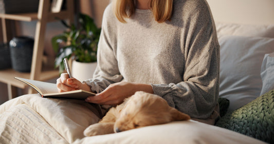 Woman journaling in bed during a quiet morning, practicing burnout recovery journaling and stress relief without pressure or perfection.