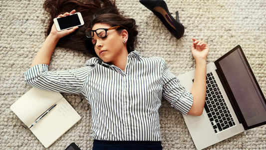 Busy professional woman overwhelmed by work stress laying on the floor with her laptop and work things scattered around her. In need of mindfulness exercises for adults who feel overwhelmed as a way to combat work stress.
