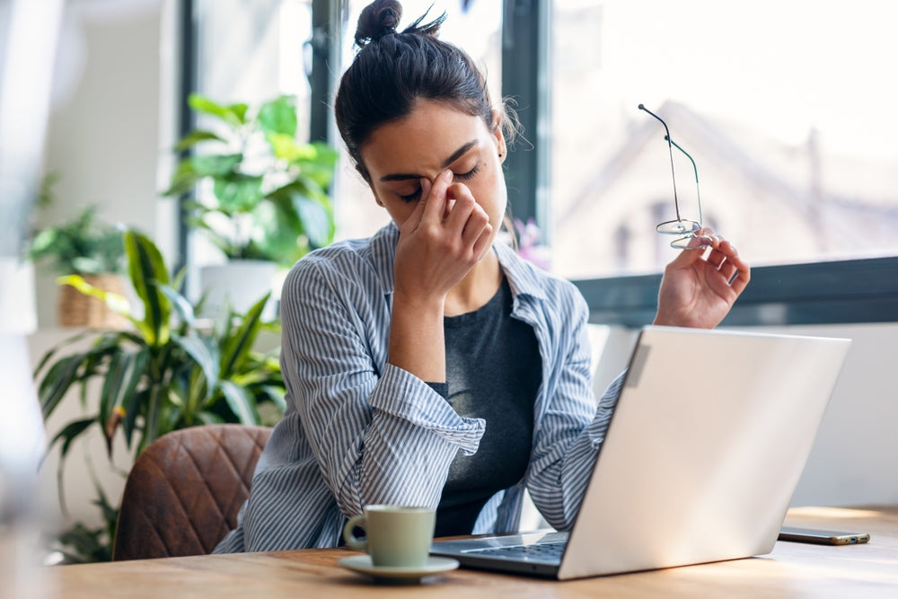 Woman experiencing exhaustion, fatigue, and burnout at a desk with laptop and coffee.
