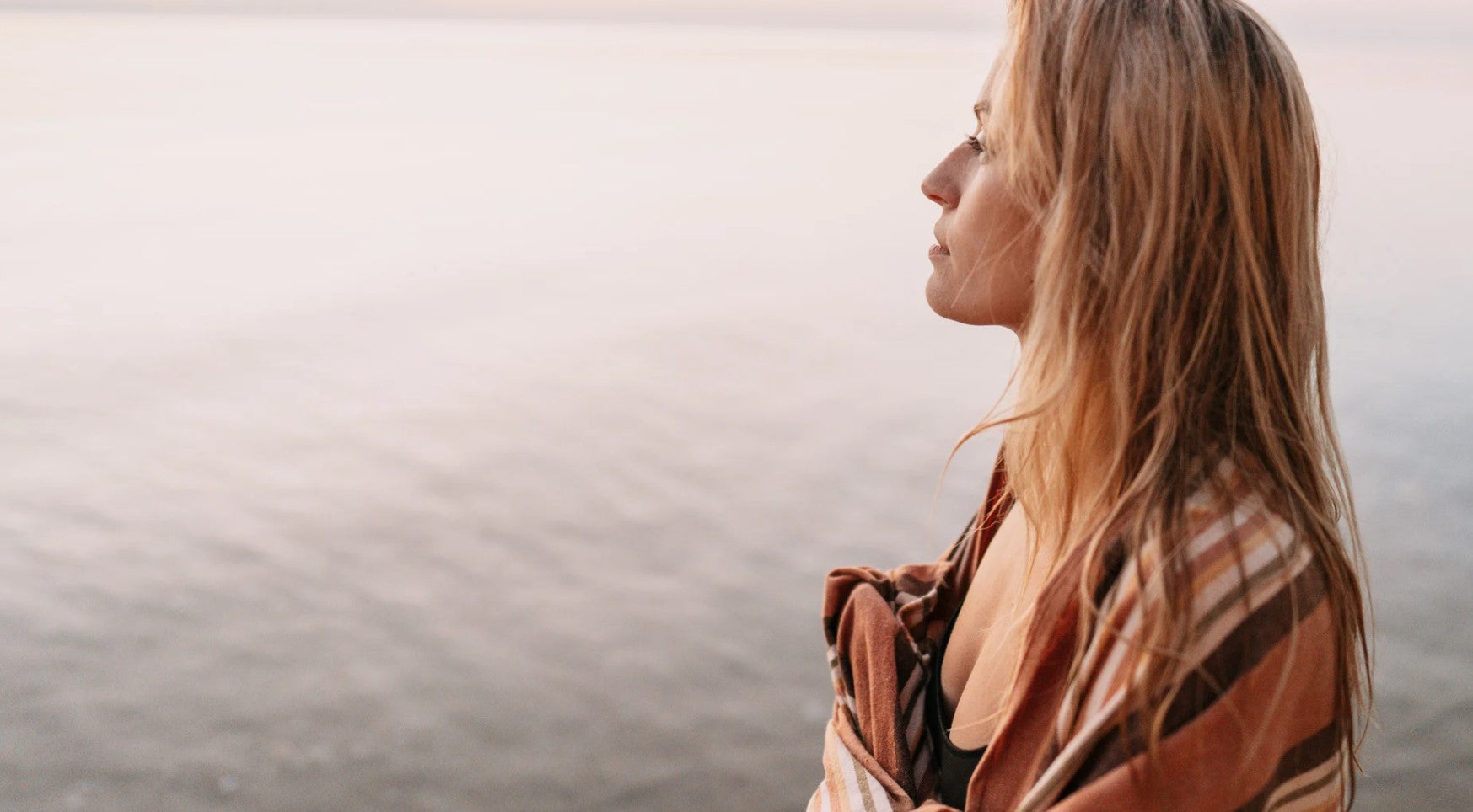 Woman with long blonde hair wearing a patterned scarf against a neutral background looking out across the calm waters