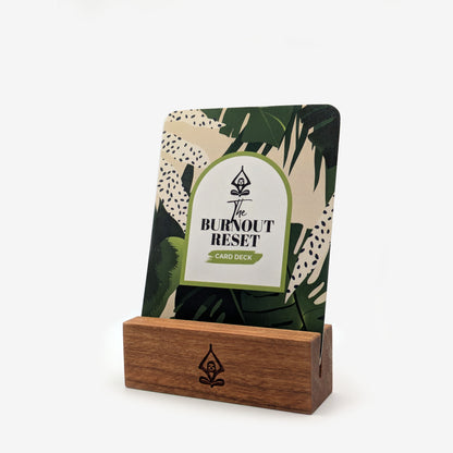 A mindful affirmation card deck titled 'The Burnout Reset' on a displayed in a handcrafted solid natural cherry wood card stand with Tranquilivia's Olivia meditation sloth logo on a white background.
