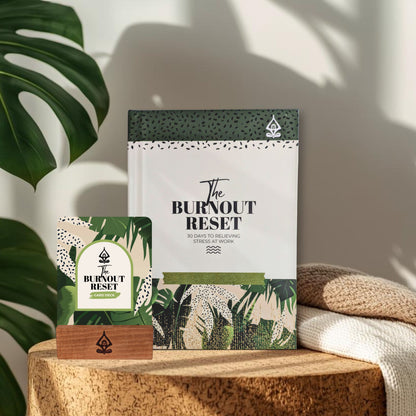 Product lifestyle for 'The Burnout Reset Journal and Card Deck Set' on a wooden surface with a plant in the background