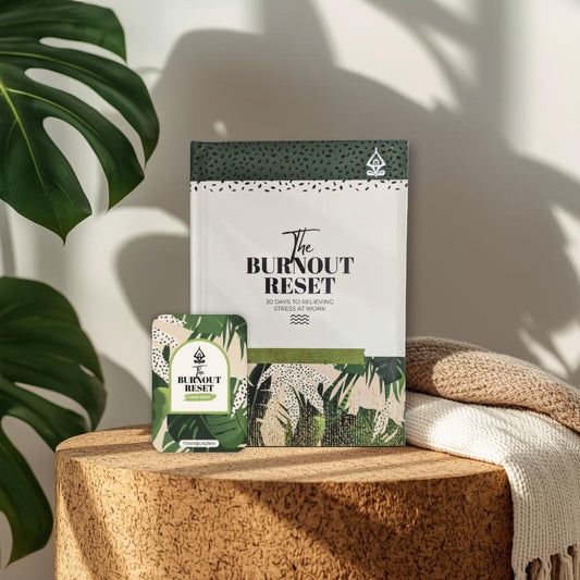 Product lifestyle for 'The Burnout Reset Journal and Card Deck Set' on a wooden surface with a plant in the background