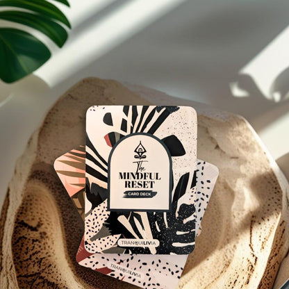 A card deck with mindful practices to support daily calm and stress relief with natural leaf design and 'The Mindful Reset' text laying flat on natural wood with a plant in the background